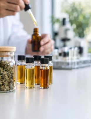 Researcher handling dropper bottle near jars of hemp flower in bright lab